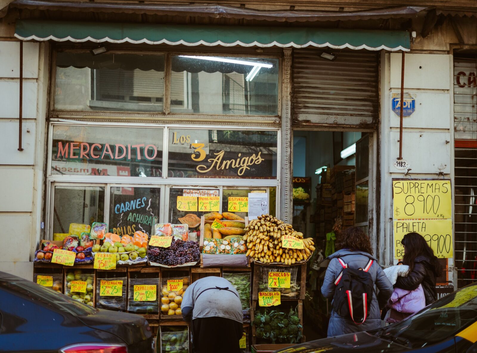 Street view of a local market 'Los Tres Amigos' in Buenos Aires with people shopping for fresh produce.