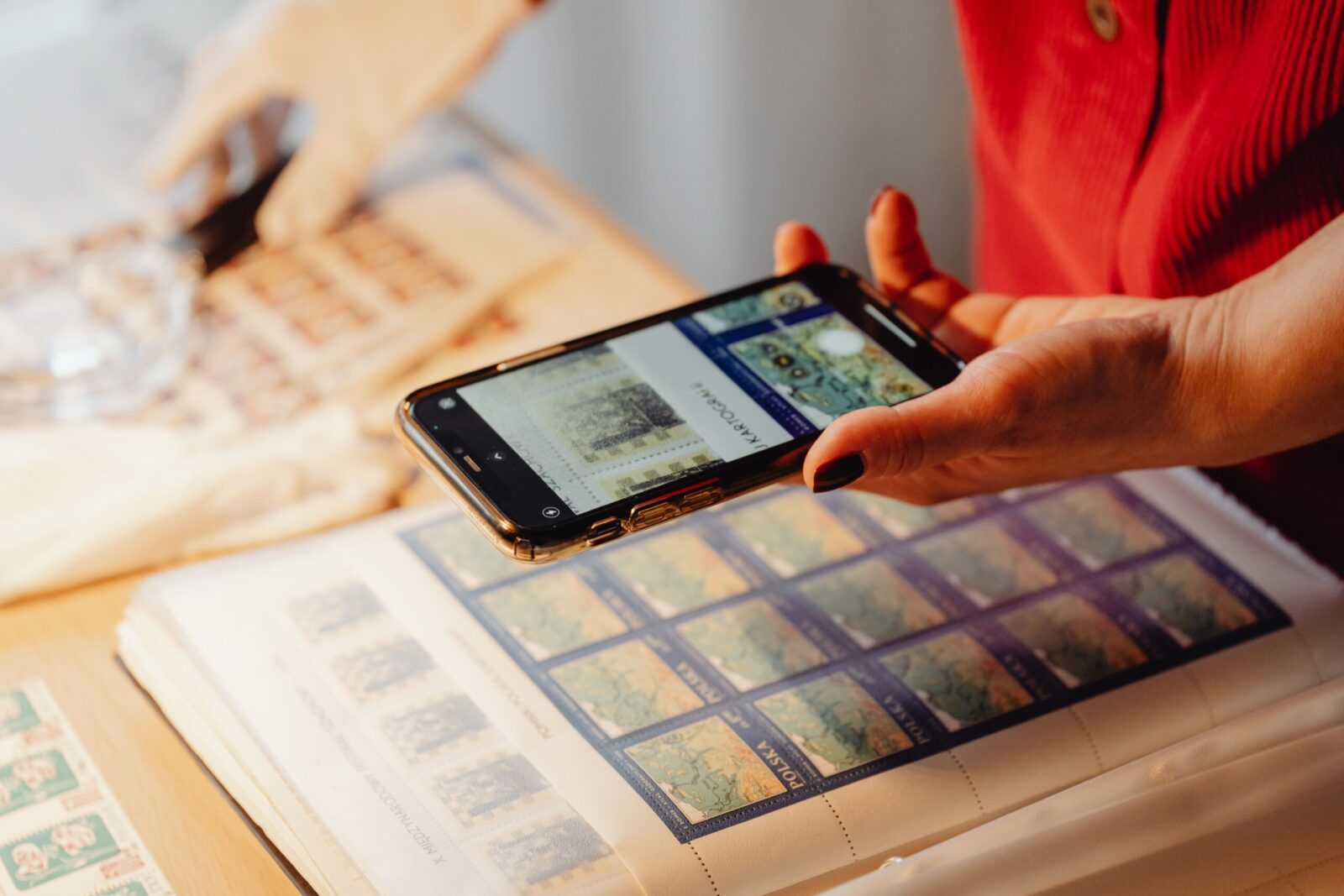 Individual photographing a stamp collection using a smartphone for cataloging.
